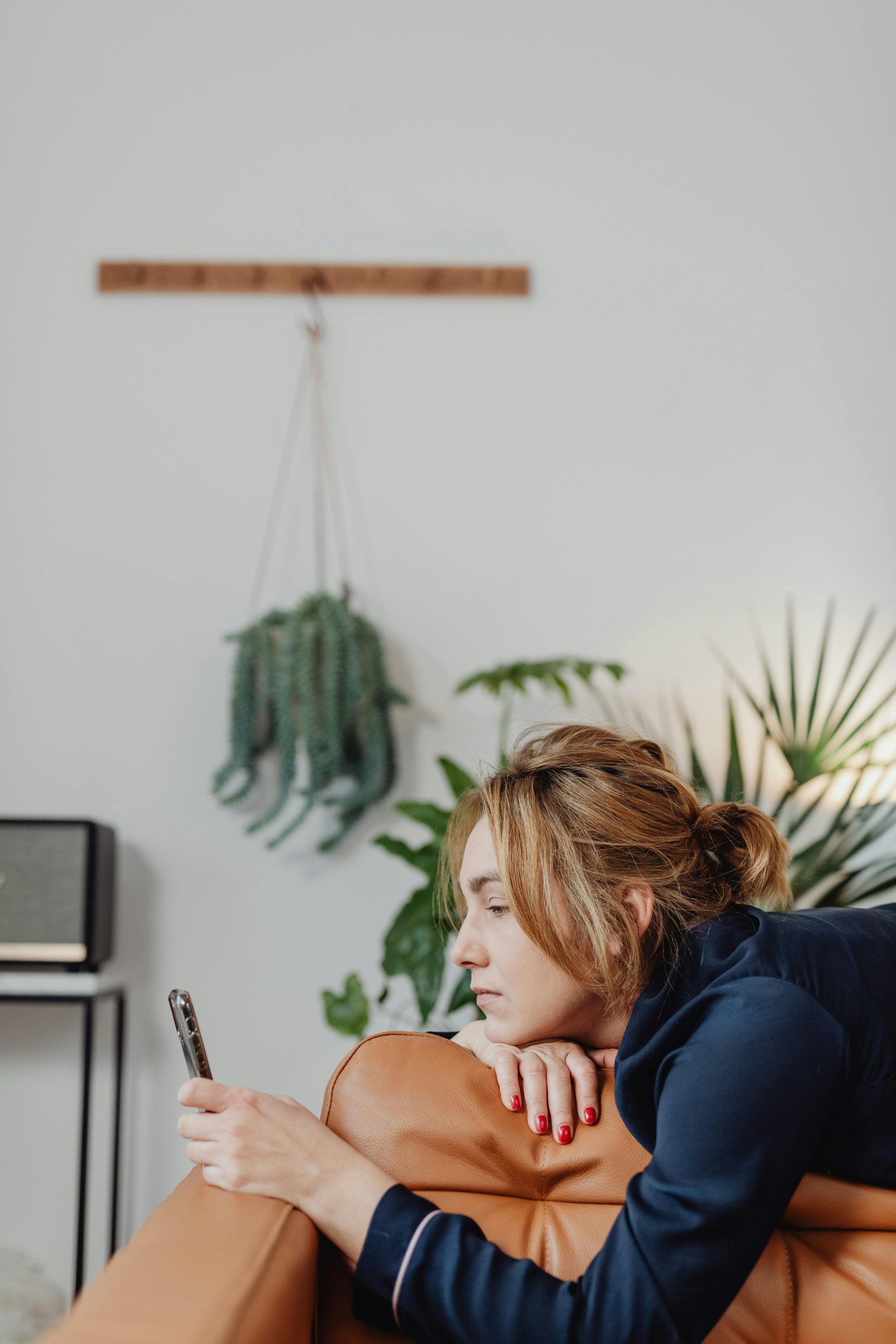 Femme allongée sur un canapé marron, regardant son portable